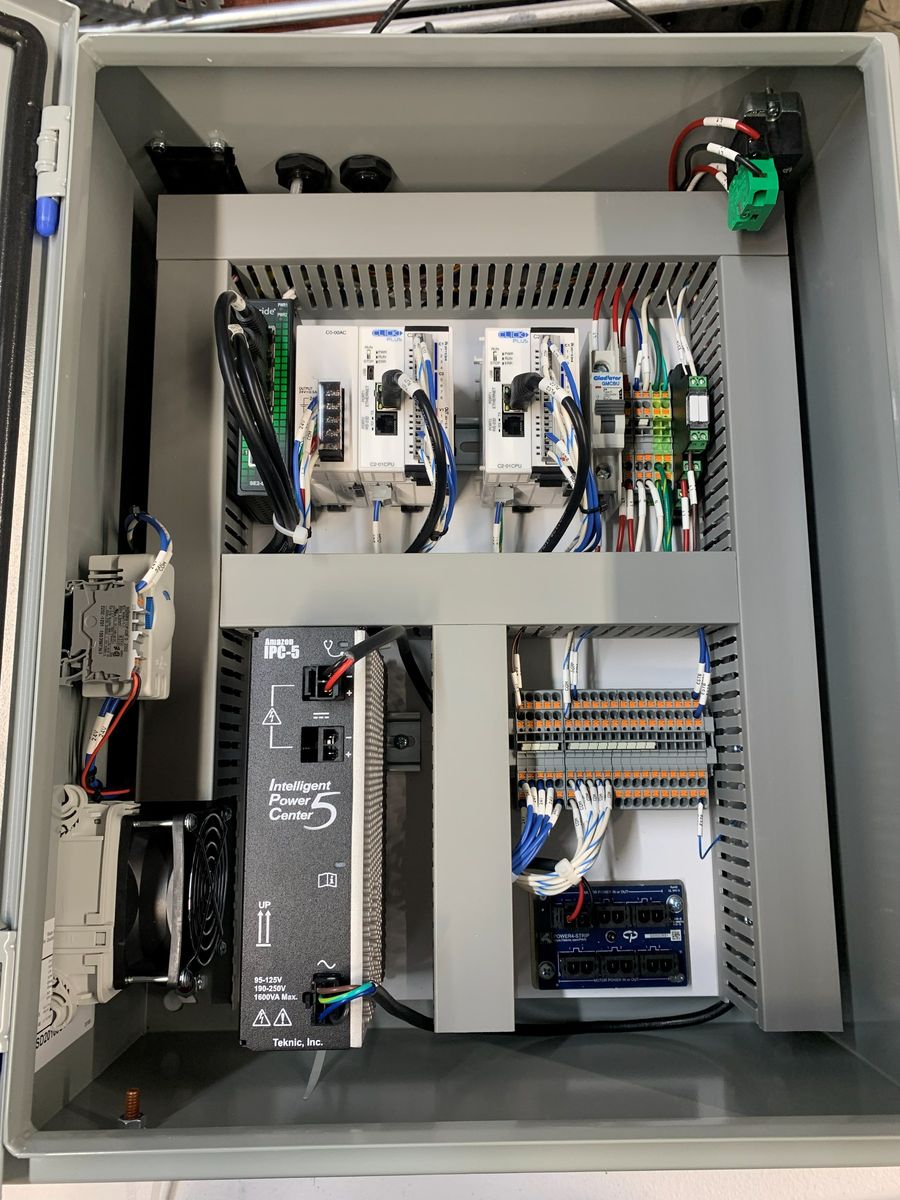 An open control panel enclosure wired in-house, showing DIN-rail mounted drives, PLC hardware and routed wiring.