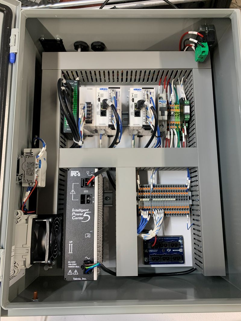 An open control panel enclosure wired in-house, showing DIN-rail mounted drives, PLC hardware and routed wiring.