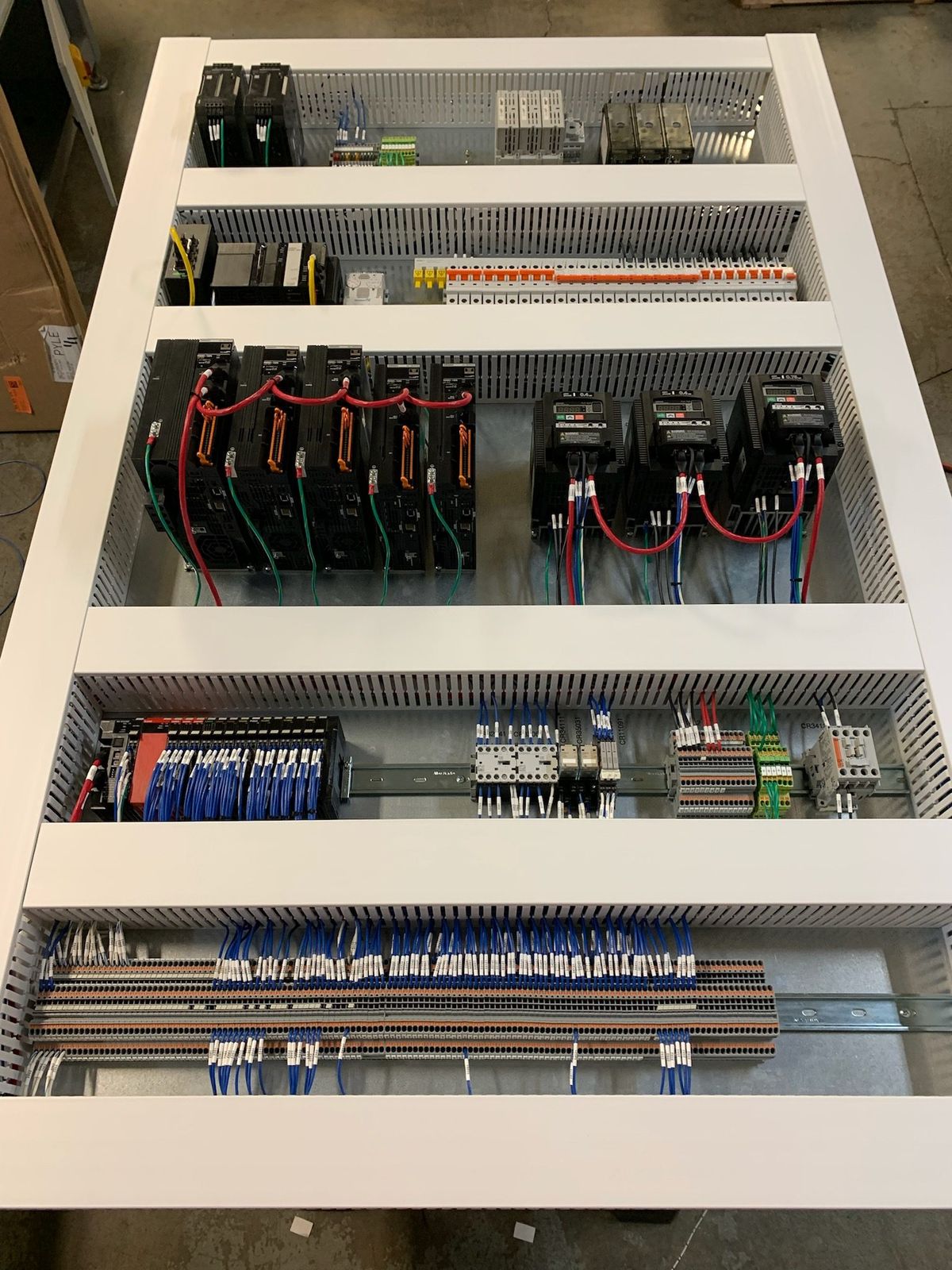 A finished control panel wired in-house — servo drives, PLC and I/O on DIN rail, with every conductor run in wire duct and landed on numbered terminals.