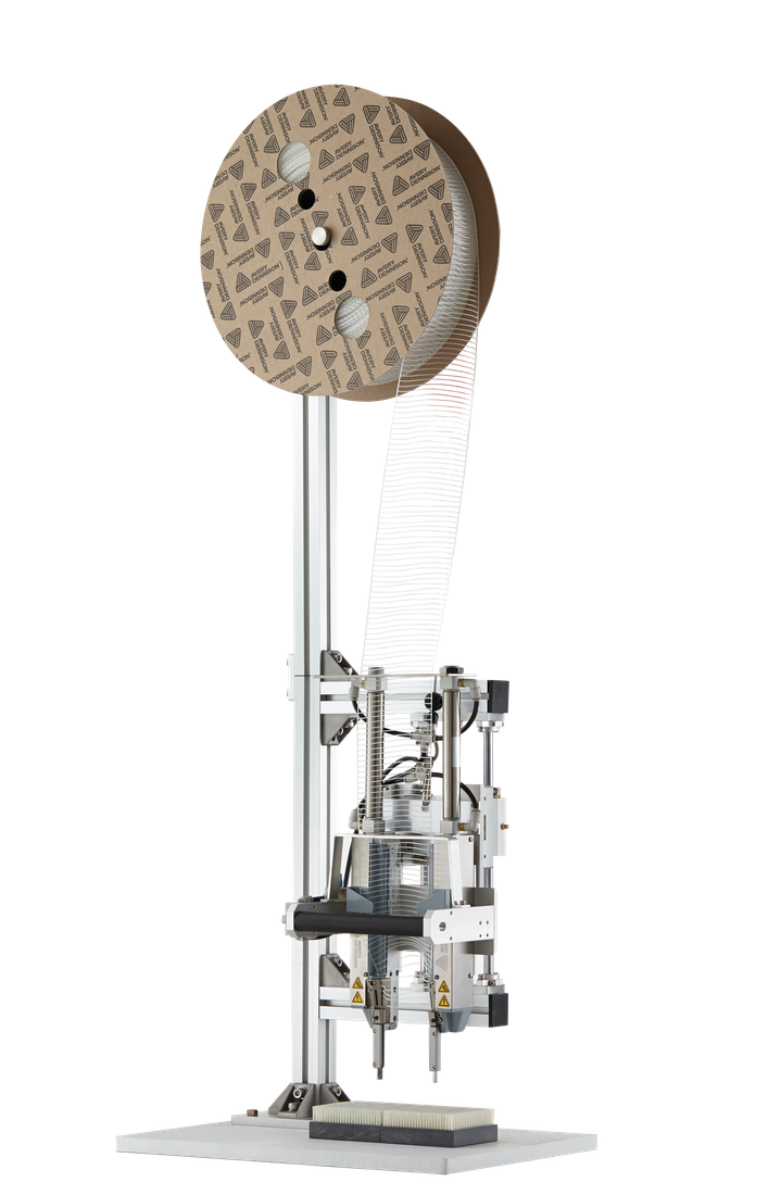 The Avery Dennison IndES Industrial Elastic Staple system on its column stand, with a reel of elastic staples feeding down to the applicator head and twin needles above a brush-back bed.