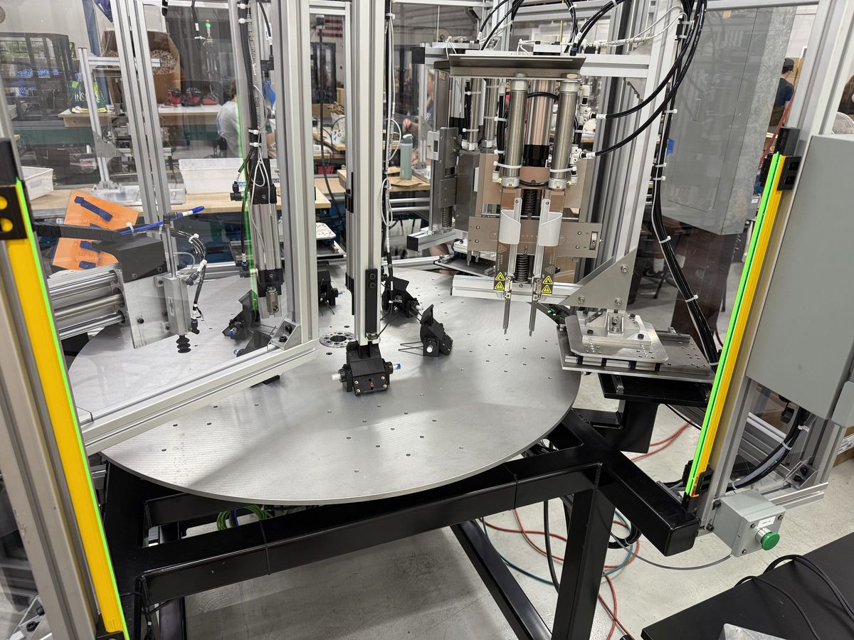 A rotary indexing cell with safety light curtains standing at the operator face and aluminum extrusion guarding enclosing the table.