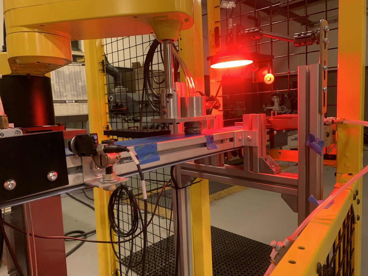 A vision inspection station lit by a red LED ring, with the camera and optics mounted on a rail above the part fixture inside a guarded cell.